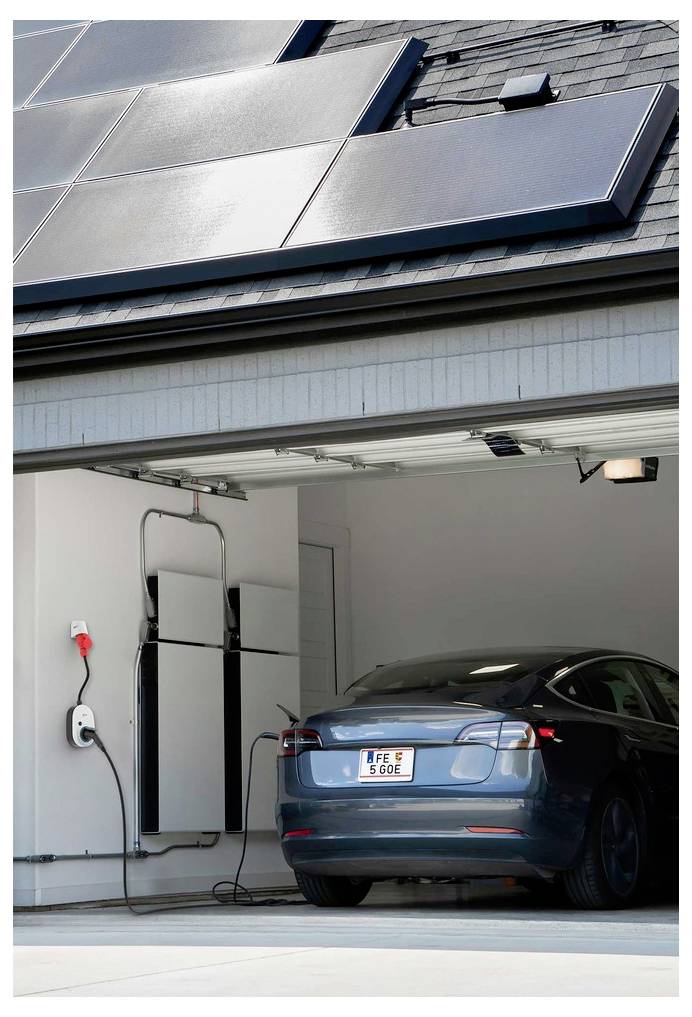 Elektrisches Auto geparkt in einer Garage mit an der Wand montierter Ladeausrüstung, unter Dachsolarpanelen.