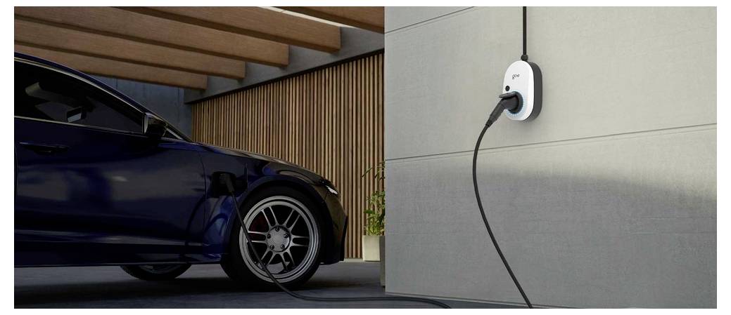 Elektroauto, das an einer wandmontierten Ladestation in einer modernen Hausgarage angeschlossen ist, mit sichtbarem Vorderrad des Fahrzeugs und Ladekabel.