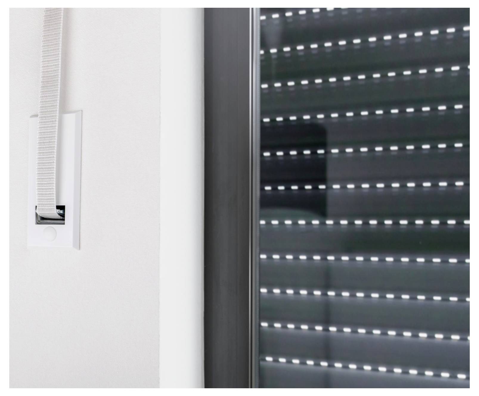 Nahaufnahme einer wandgestützten Bedienungsvorrichtung für eine Rollorollo neben einem Fenster mit einem teilweise geschlossenen äußeren Rollladen.