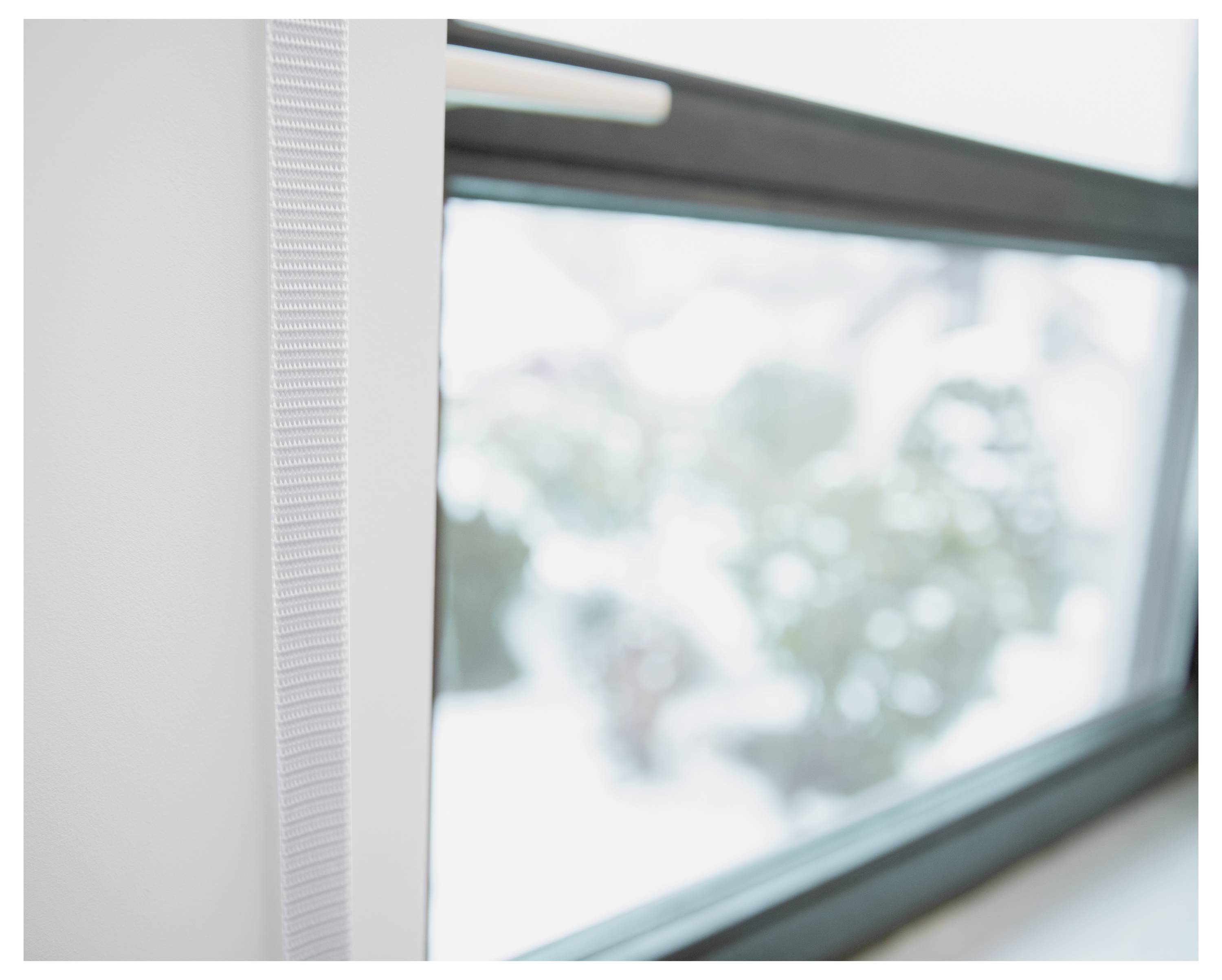 Nahaufnahme eines Fensterrahmens mit einem eingebauten vertikalen Jalousien- oder Schirmsystem, mit unscharfer Außenansicht hinter dem Glas.
