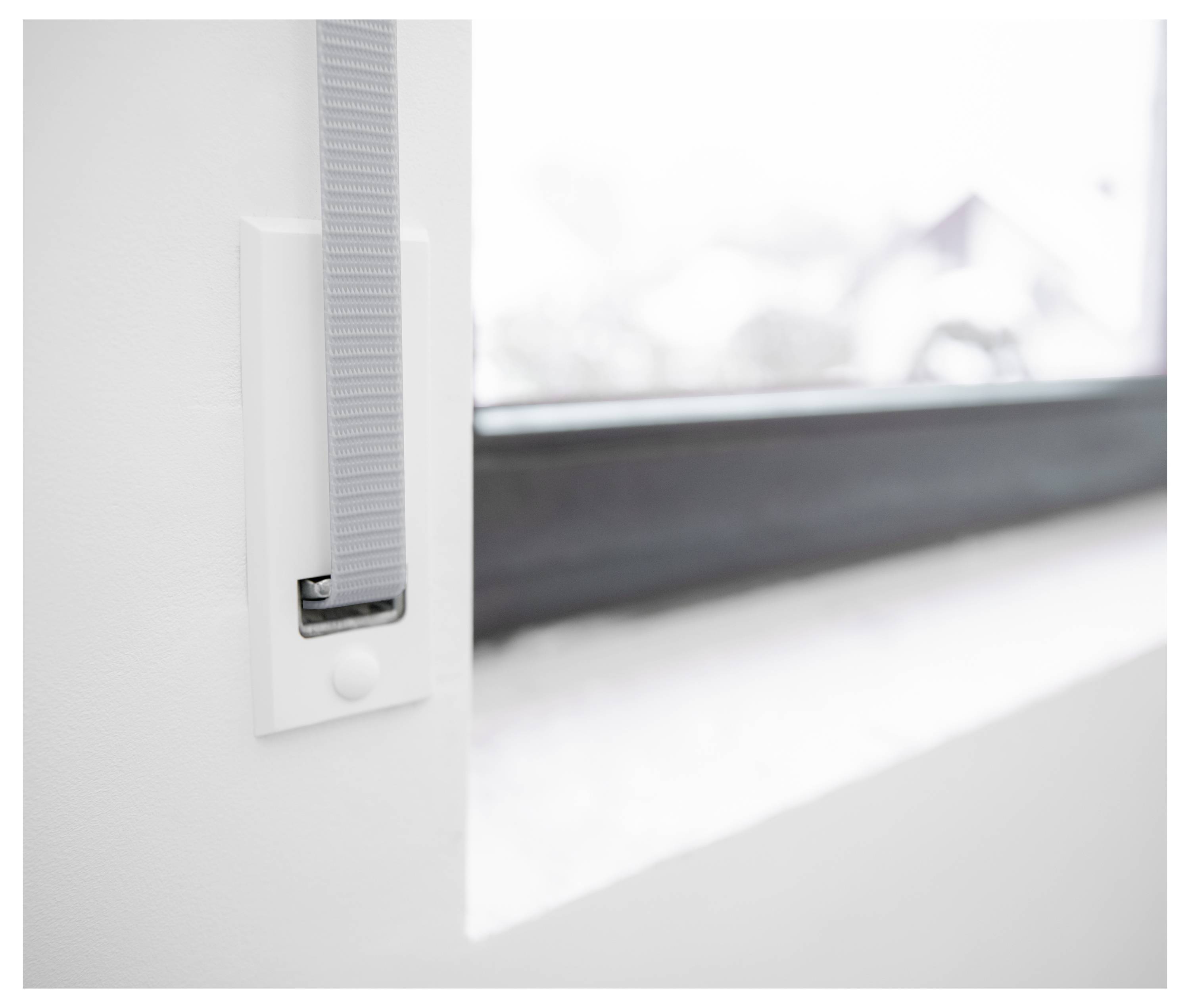 Nahaufnahme eines Fensterriegel und Zugbandes an einem weißen Rahmen, mit verschwommener, heller Außenansicht hinter dem Glas.