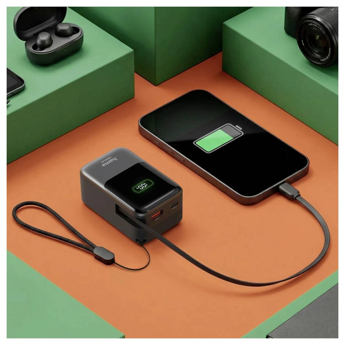 Ein Smartphone, das neben einer kompakten Powerbank auf einer orangefarbenen Oberfläche aufgeladen wird, mit einem grünen Batteriesymbol auf dem Telefonbildschirm angezeigt.