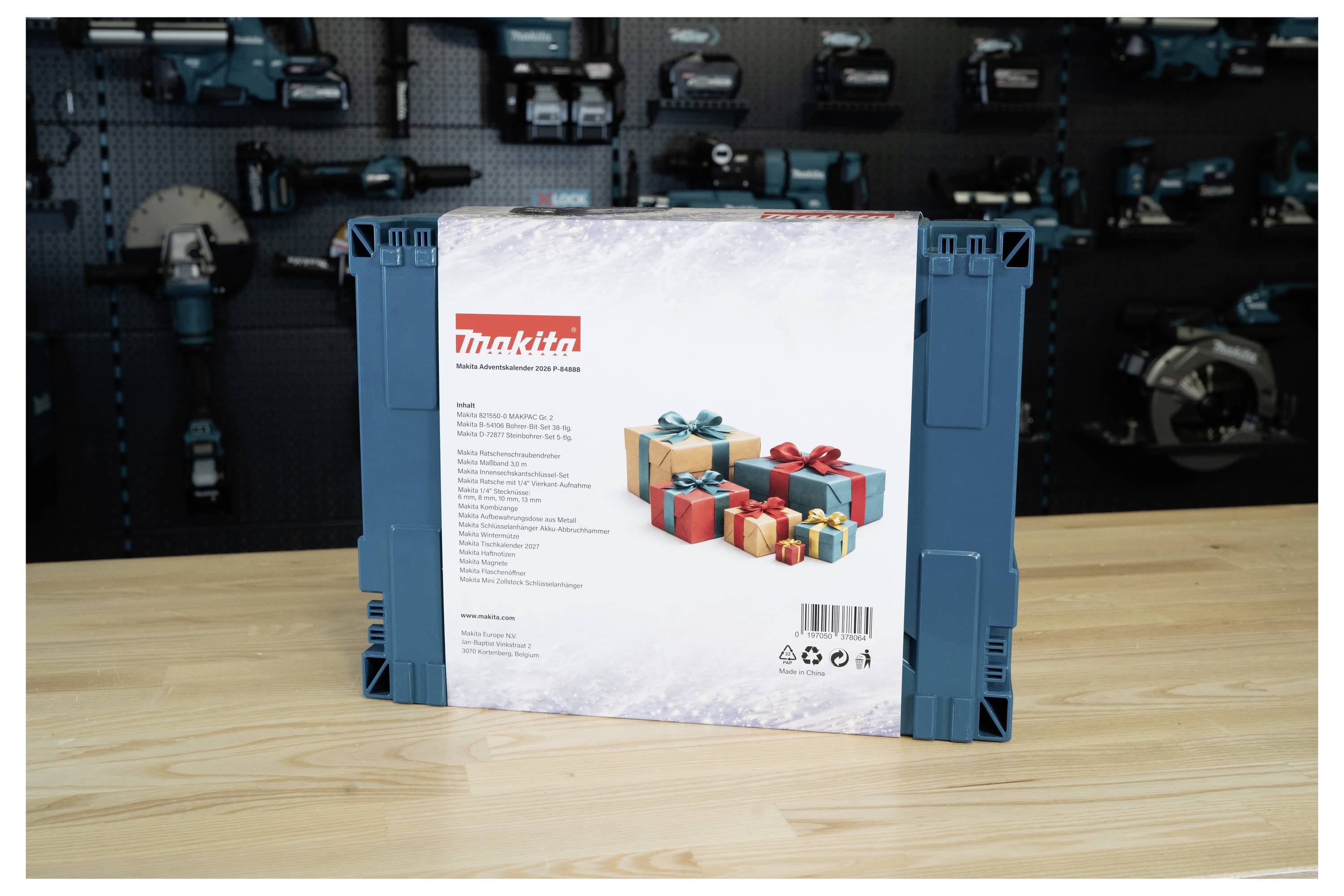 Ein in einer Box verpacktes Makita-Werkzeugset oder -koffer, aufrecht auf einem Holztisch vor einer unscharfen Wand mit Elektrowerkzeugen dargestellt.