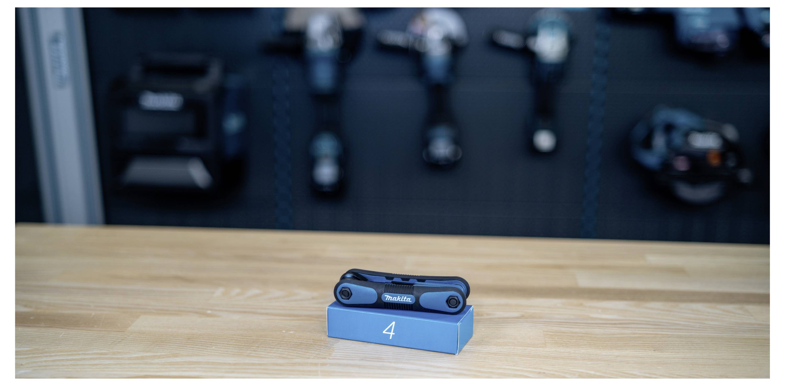 Ein blaues Taschenmesser zum Zusammenklappen ruht auf einem nummerierten Anzeigeblock auf einem Holztisch, mit unscharfem Fitness-Zubehör im Hintergrund.
