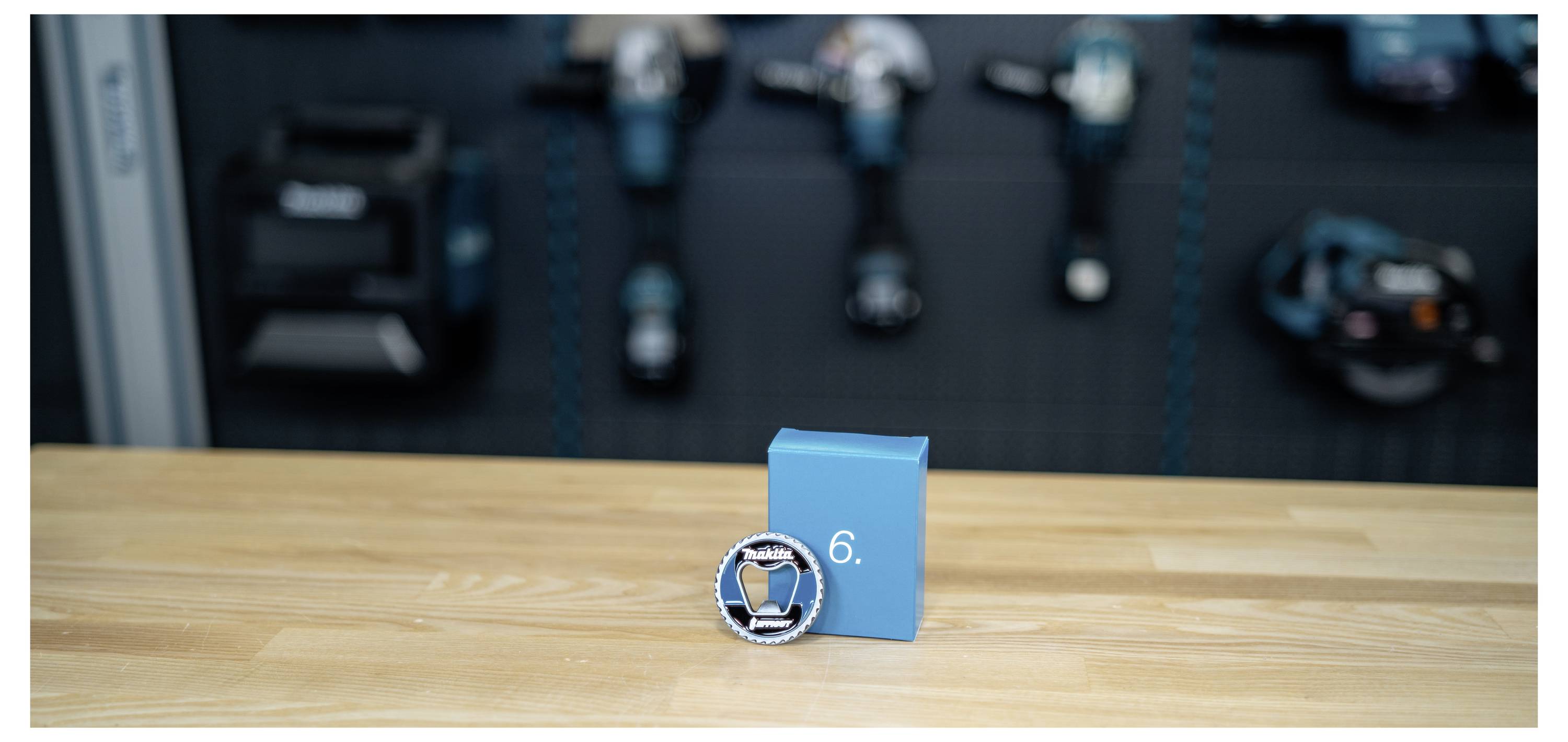 Blaue Auszeichnungsbox mit einer runden silbernen und blauen Medaille mit der Markierung 6 auf einem Holztisch, mit unscharfem Trainingsgerät im Hintergrund.
