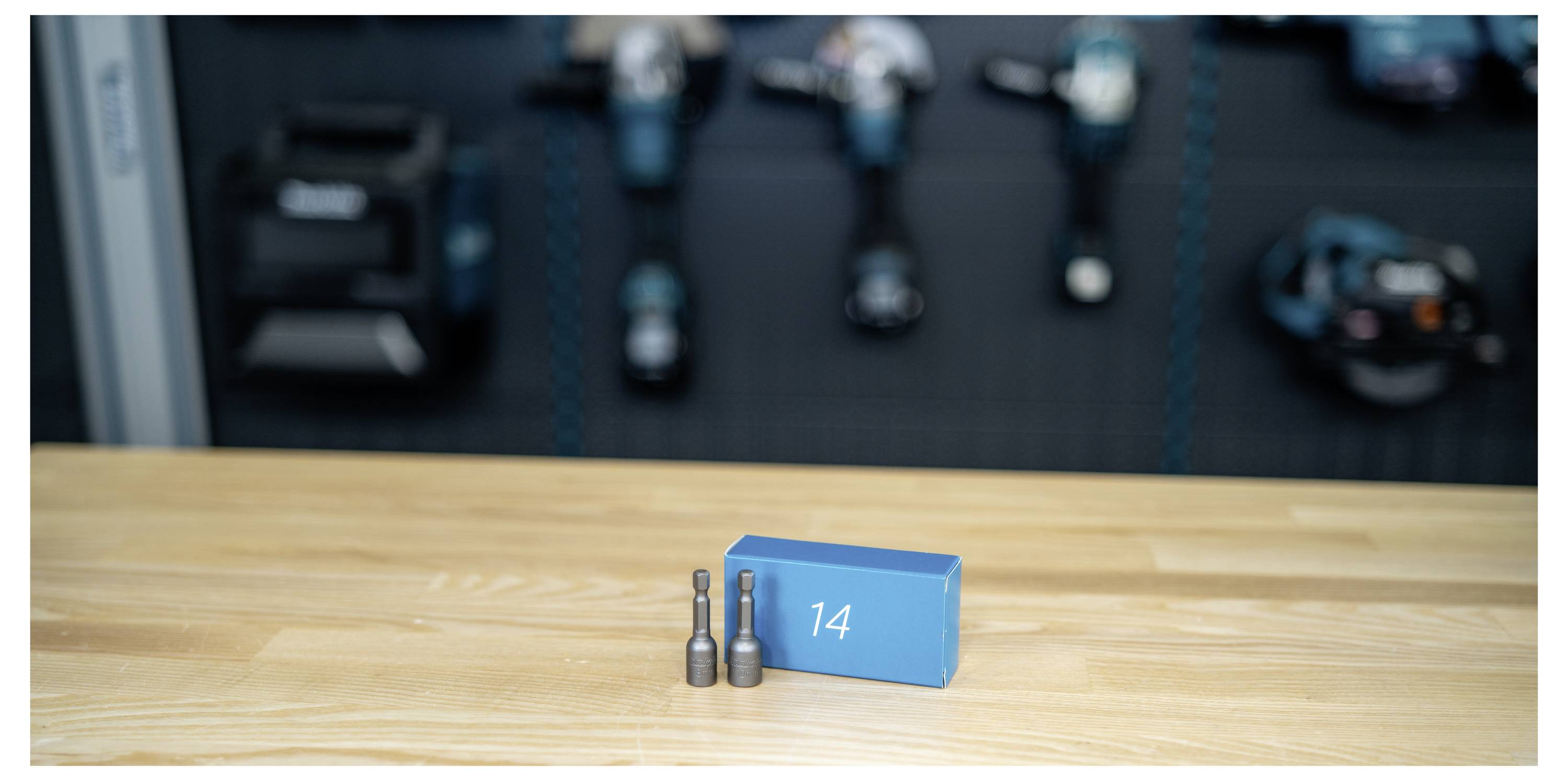 Nummerierter blauer Block '14' mit zwei Metallbolzen auf einem Holztisch, mit unscharfer Industriemaschine im Hintergrund.