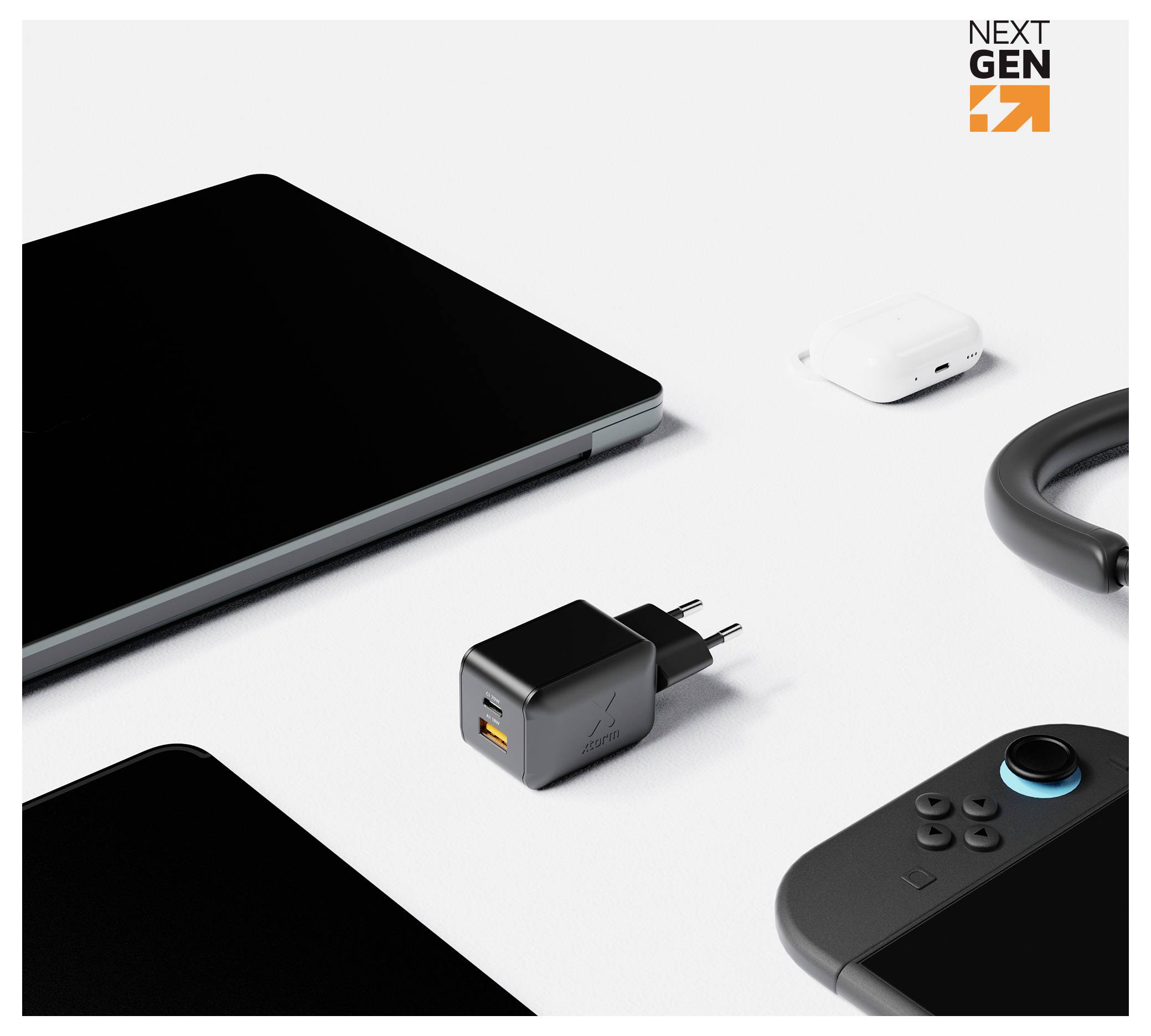 Sortierte Technologiegeräte auf weißem Hintergrund, zentriert auf einem schwarzen USB-Wandladegerät mit orangefarbigem Anschluss; Laptop, Kopfhöreretuui, Kabel und Spielecontroller in der Nähe.