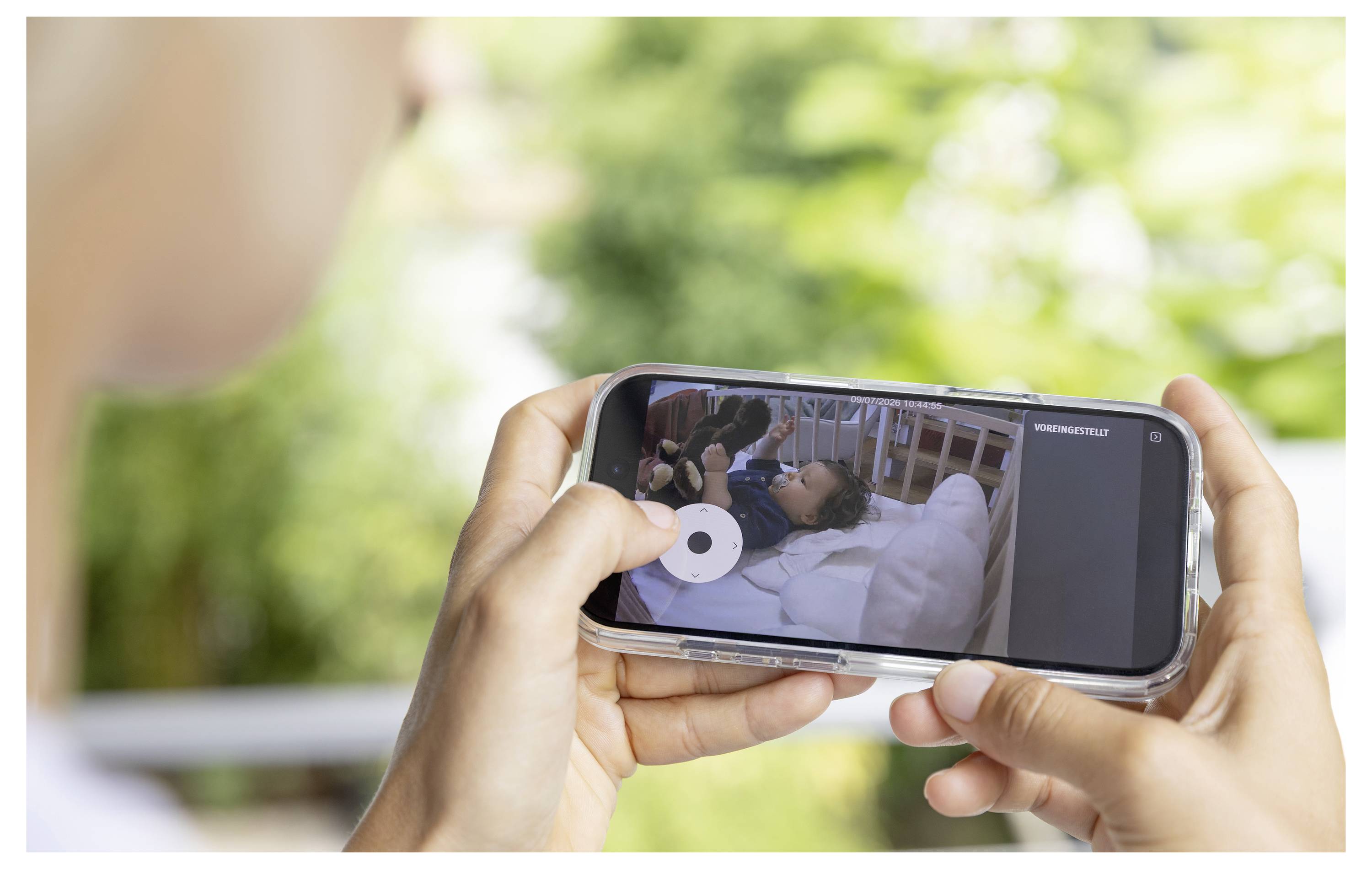 Person, die ein Smartphone hält, auf dem ein Video einer Person zu sehen ist, die in einem Krankenhausbett liegt, von außen vor einem unscharfen grünen Hintergrund betrachtet.