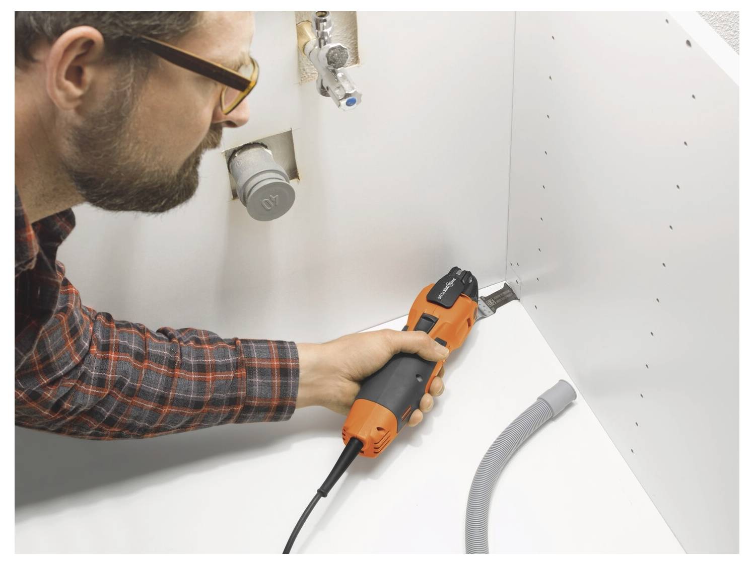 Ein Mann benutzt einen orangefarbenen Elektroschrauber, um eine Schraube in ein weißes Schrank- oder Wandpaneel während der Heimwerkermontage einzudrehen.