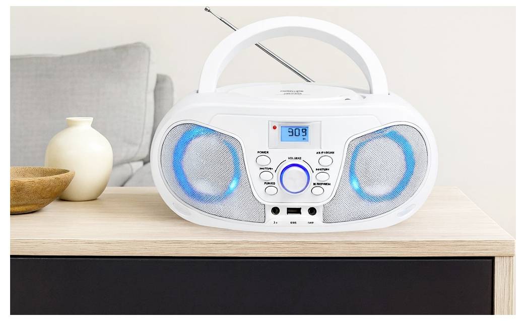 Tragbarer weißer Boombox mit blau beleuchteten Lautsprechern und digitaler Anzeige auf einem Holztisch, mit erhöhter Teleskopantenne dahinter.