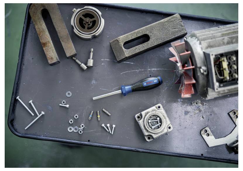 Zerlegte mechanische Teile und Werkzeuge auf einer Werkbank verteilt, einschließlich eines Schraubenziehers, Bolzen, Blöcken und eines roten Lüfterflügels.