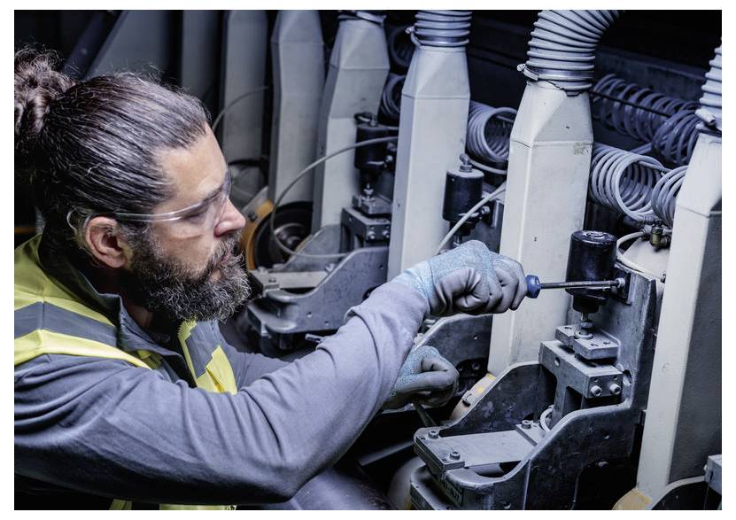 Ein Techniker trägt eine Schutzbrille und Handschuhe und repariert elektrische Maschinen mit einem Schraubendreher in industriellen Geräten.