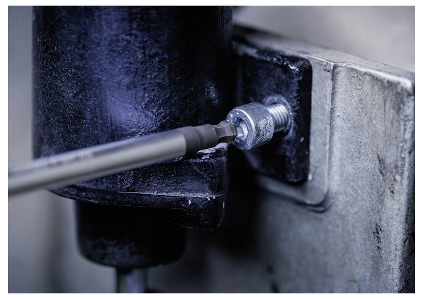 Nahaufnahme eines Schraubendrehers, der eine Schraube an einem schwarzen Metallscharnier festzieht, das auf einer Beton- oder Steinoberfläche montiert ist.