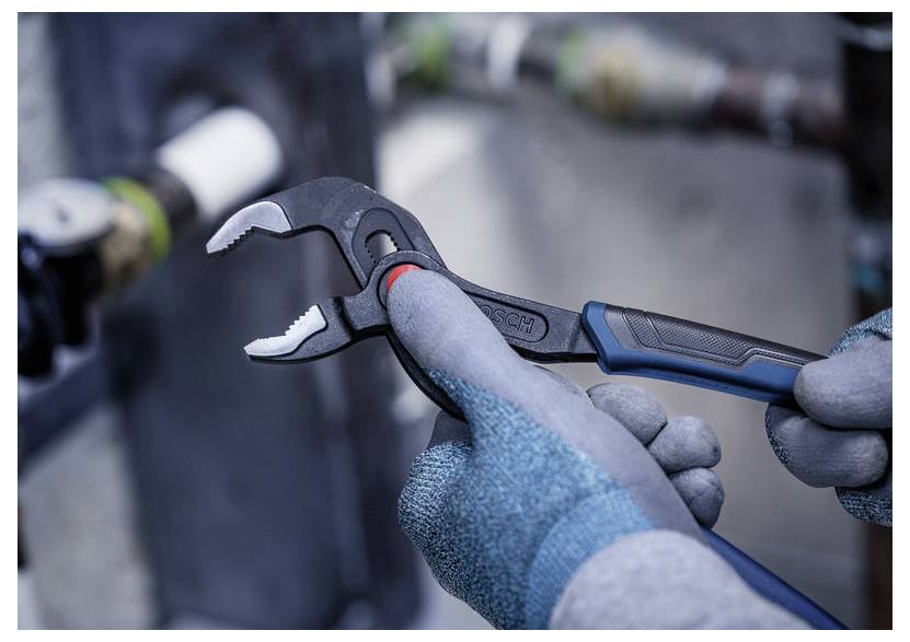 Handschuhe tragende Hände stellen einen blau-schwarzen Verstellschlüssel an einer Metallfitting in einer industriellen Umgebung ein.