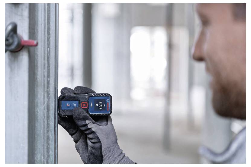 Ein Arbeiter nutzt ein tragbares digitales Laserentfernungsmessgerät, um die Entfernung an einem Metallwandrahmen auf einer Baustelle zu messen.