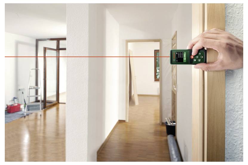 Tragbares Laser-Entfernungsmessgerät, das eine rote Linie durch einen Flur in einem unfertigen Raum projiziert und die Wand-zu-Wand-Entfernung misst.