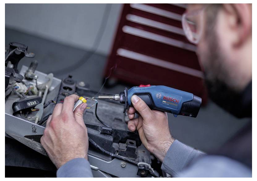 Techniker, der einen kabellosen Bosch-Schraubendreher verwendet, um Maschinen auf einer Werkbank zu reparieren, mit Händen konzentriert auf ein kleines Bauteil.