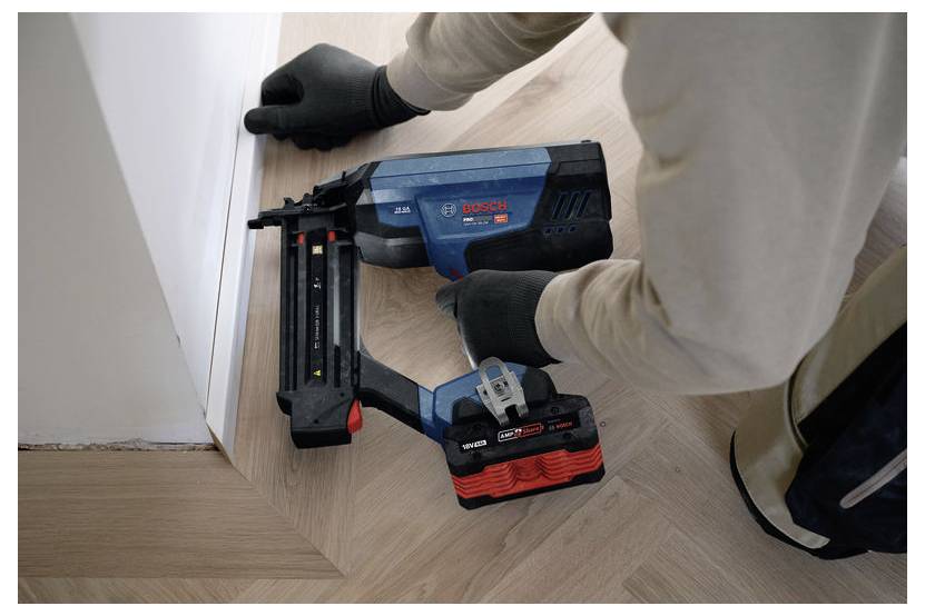 Ein Arbeiter verwendet einen kabellosen Bosch-Nagler, um Zierleisten an einer Wandecke in einem Wohnungsinneren zu befestigen.