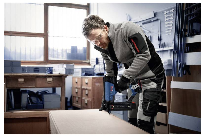 Ein Mann benutzt einen kabellosen Elektrotacker, um ein Holzstück in einer Werkstatt oder Schreinerei zusammenzubauen.