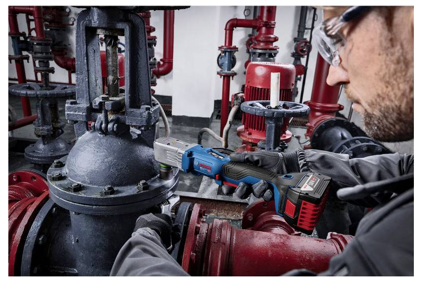 Techniker, der ein kabelloses Elektrowerkzeug verwendet, um ein großes Industrierohrventil in einem Maschinenraum zu reparieren.