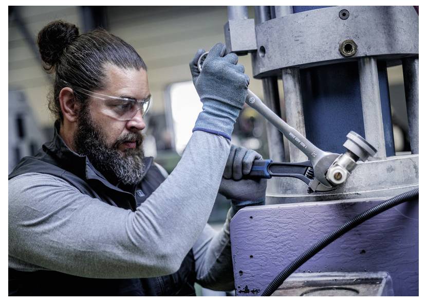 Ein Techniker trägt Schutzbrille und Handschuhe und verwendet einen Schraubenschlüssel, um Maschinen in einer Werkstatt einzustellen.