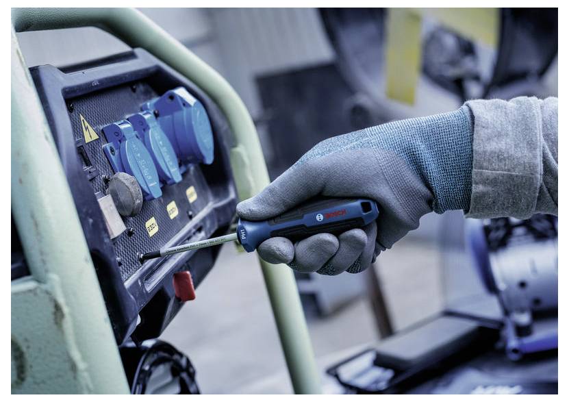 Handschuhtragender Arbeiter benutzt einen Bosch-Schraubendreher an einer Industriesteuertafel mit blauen Schaltern und Warnaufklebern.