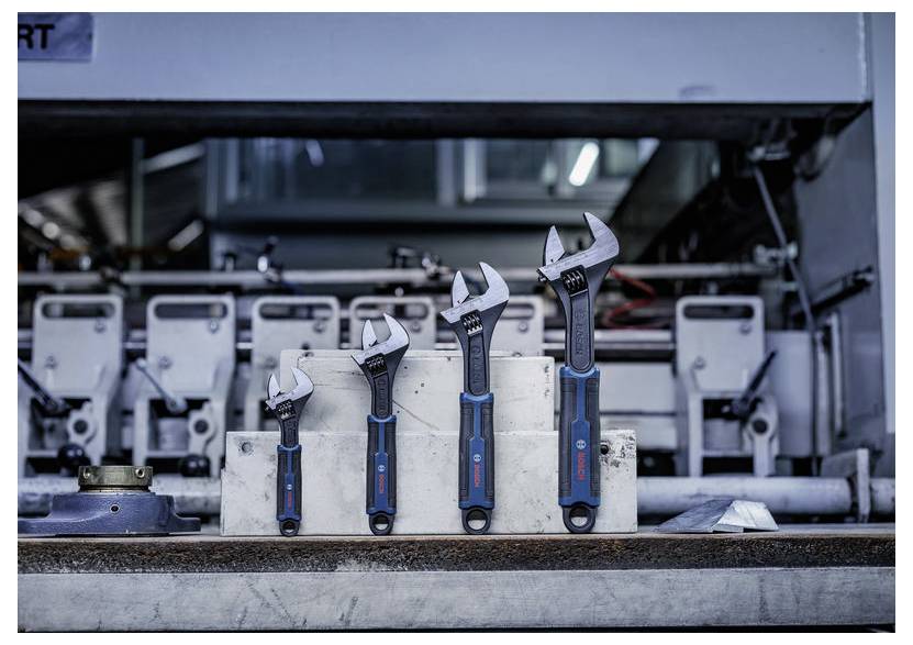 Vier verstellbare Schraubenschlüssel unterschiedlicher Größen stehen auf einer Metallplattform in einer Industriewerkstatt oder Fabrikumgebung.