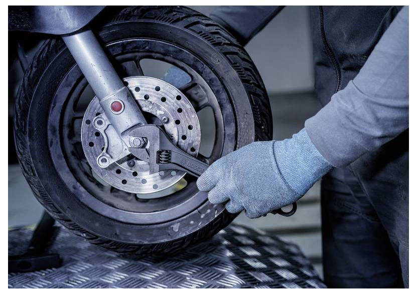 Ein handschuhschutz Mechaniker verwendet einen Schraubenschlüssel, um die Bremsanlage des Vorderrads eines Motorrads in einer Werkstatt einzustellen.
