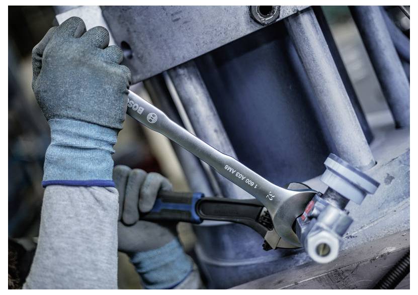 Nahaufnahme von Arbeitern mit Handschuhen, die einen Schraubenschlüssel und eine Ratsche verwenden, um eine Schraube an einer Industriemaschine festzuziehen.