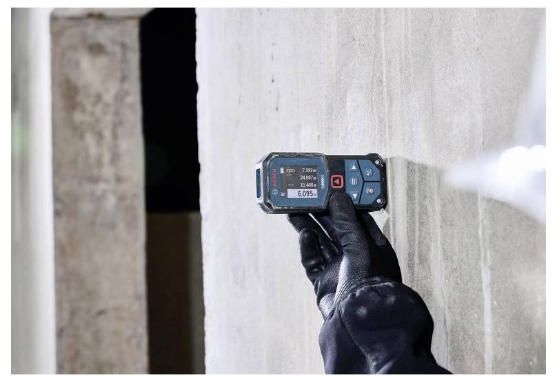 Behandschuhte Hand verwendet ein digitales Feuchtemessgerät an einer Wand, um auf Feuchtigkeit oder Wasserschäden zu prüfen.