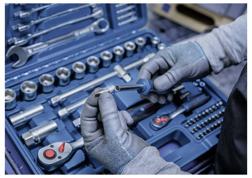 Behandschuhte Hände inspizieren eine Metallsteckdose in einem blauen Mechaniker-Werkzeugsatz mit Schraubenschlüsseln, Steckdosen und Ratschendreher, die in einem Koffer angeordnet sind.