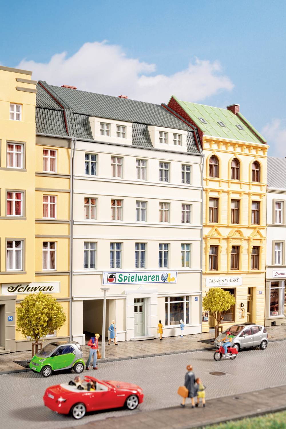 Straßenszene mit farbenfrohen europäischen Reihenhäusern mit Geschäften, Fußgängern auf dem Gehweg und mehreren Autos, einschließlich eines roten Cabriolets und eines grünen Kleinwagens.