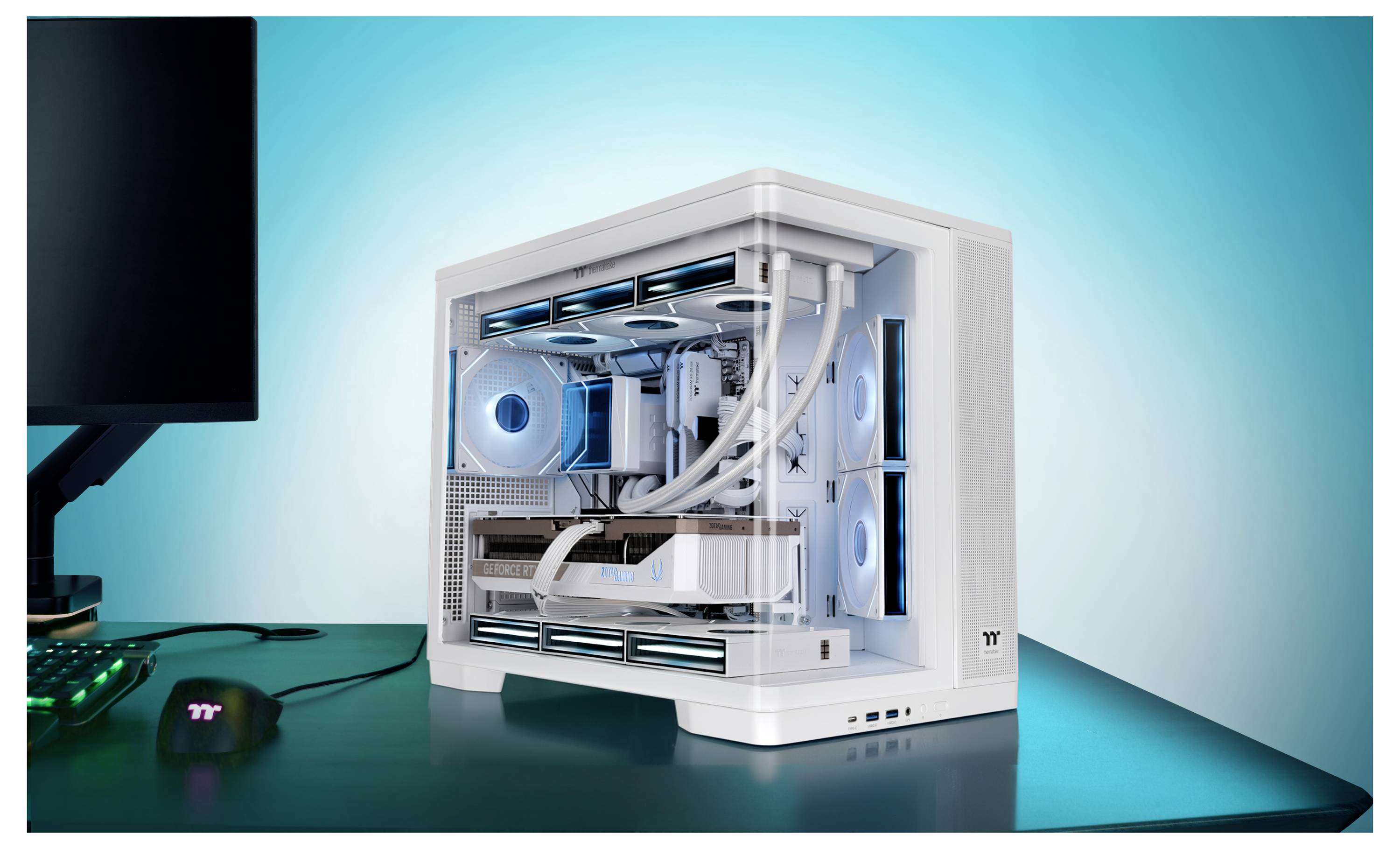 Weißer Desktop-Gaming-PC-Tower mit entferntem Seitenpanel, das blau beleuchtete Kühlungsventilatoren und interne Komponenten auf einem Schreibtisch neben einem Monitor und einer Maus zeigt.
