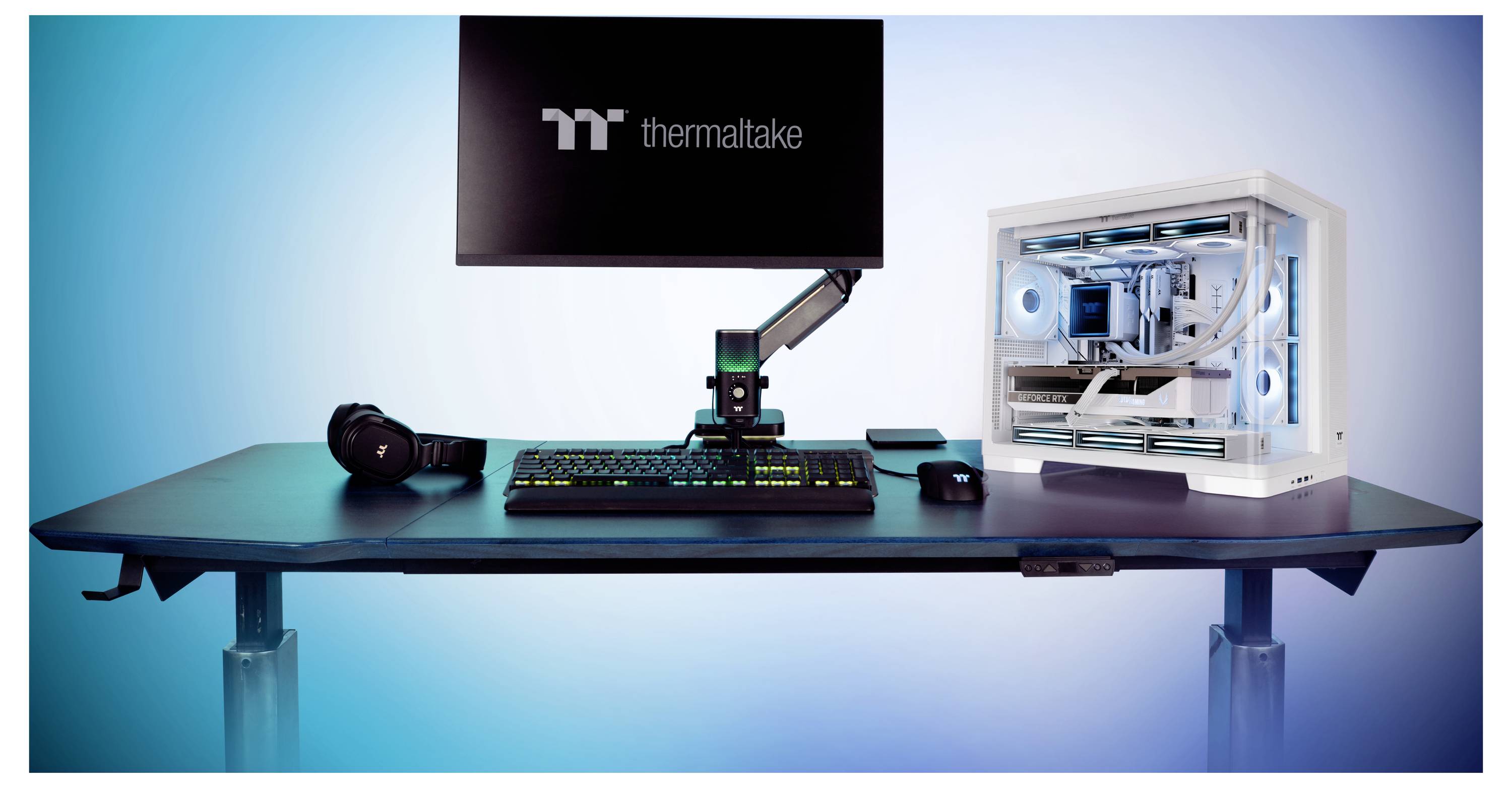 Gaming-Schreibtisch-Setup mit Thermaltake-Monitor, RGB-Tastatur und -Maus, Headset, Mikrofonarm und weißem Custom-PC-Gehäuse mit blau beleuchteten Lüftern.