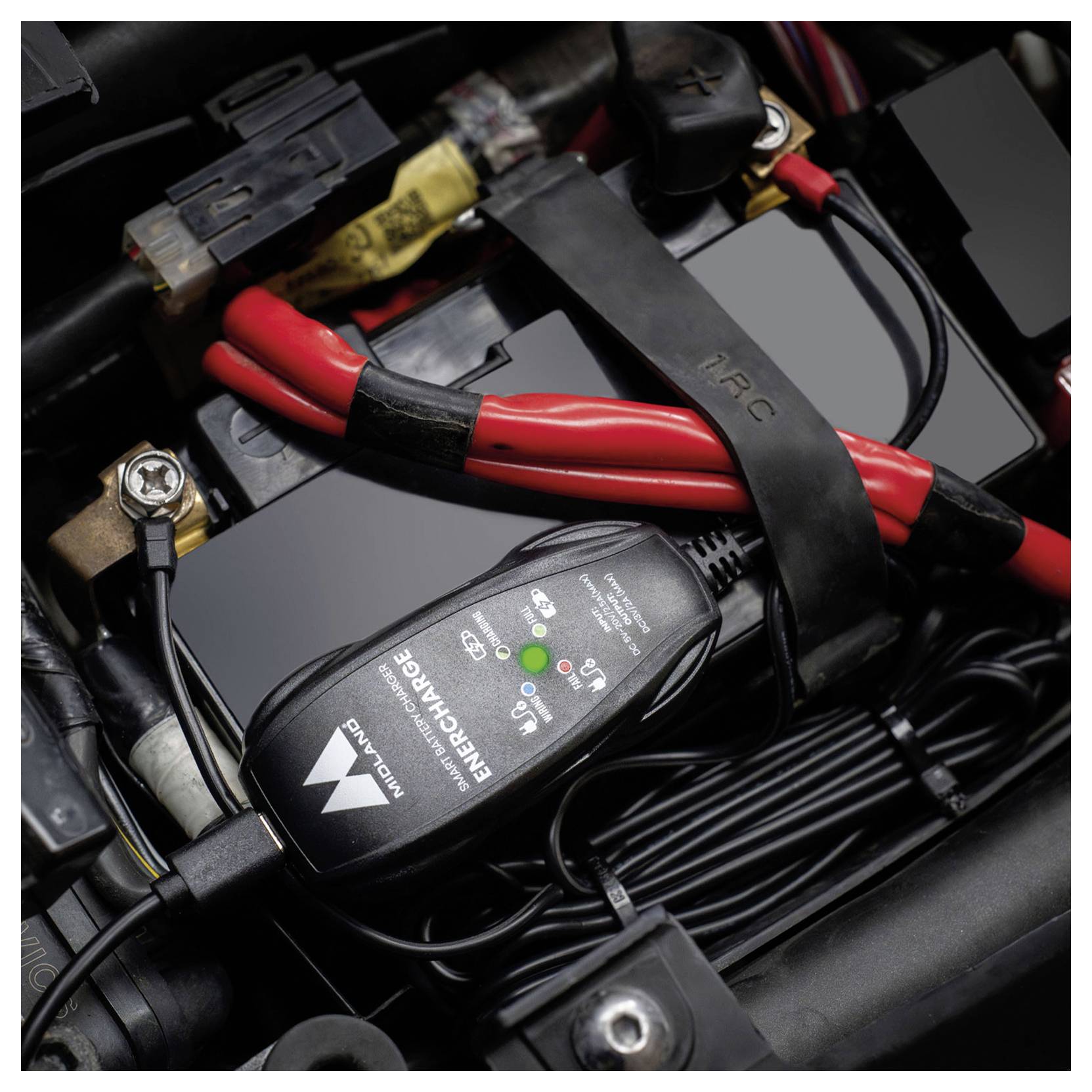 Ladegerät an eine Fahrzeugbatterie mit roten und schwarzen Kabeln und einer Ladestatus-Anzeige angeschlossen