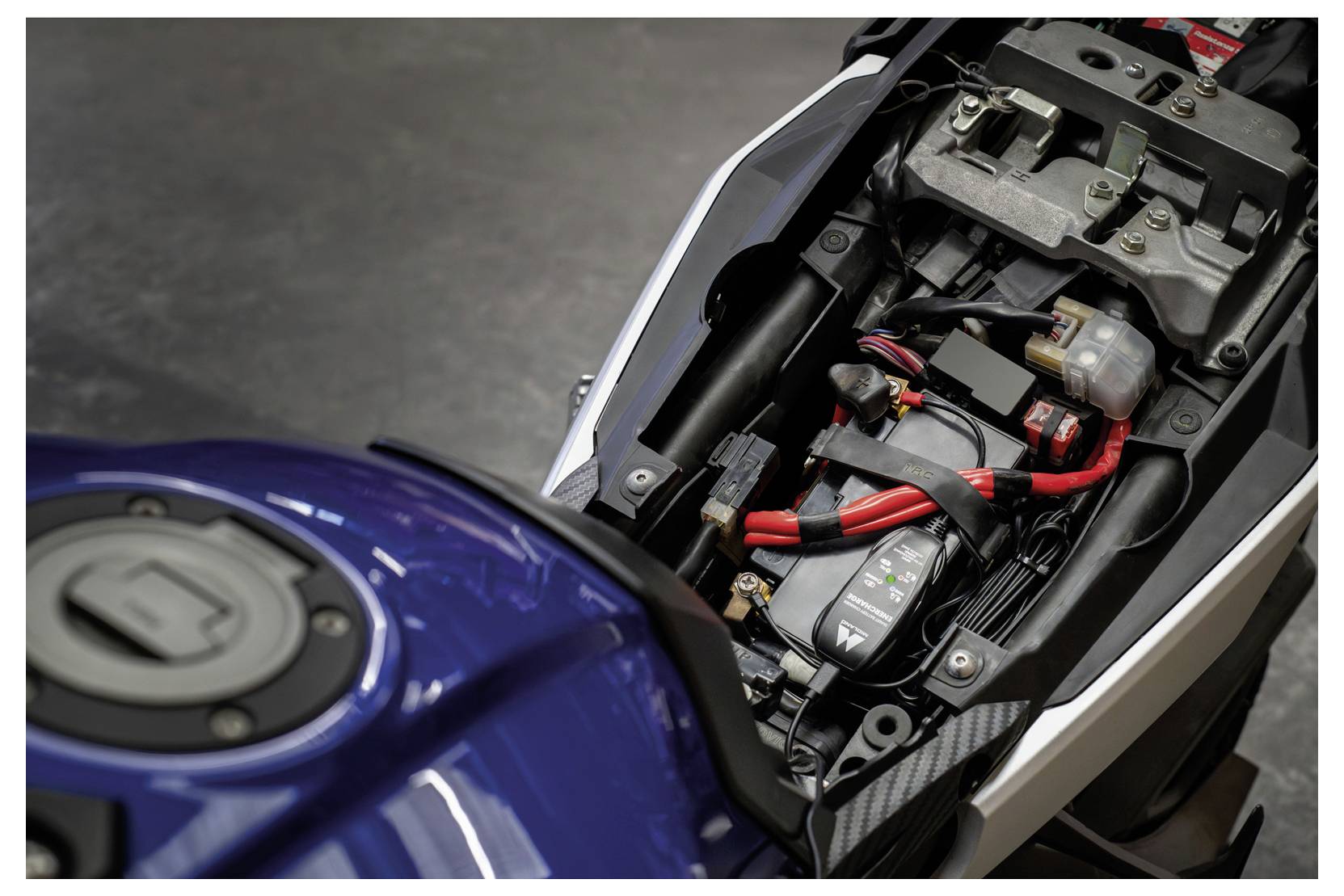 Offenes Motorrad-Sitzkastenfach mit Batterie, Verkabelung und elektrischen Komponenten unter dem Sitz.