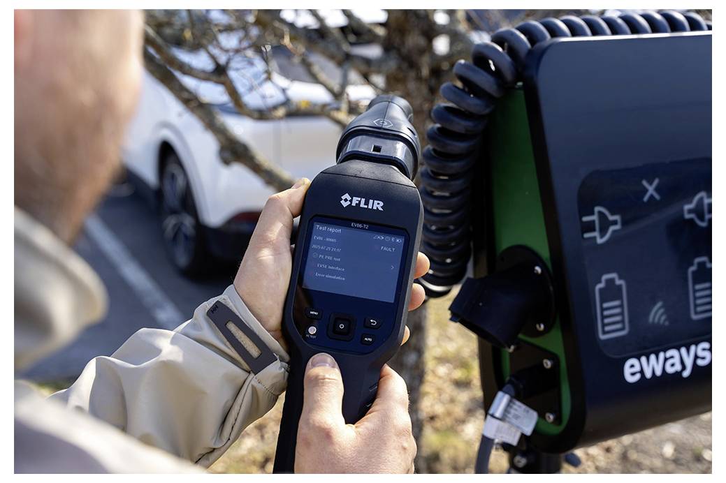 Eine Person nutzt eine FLIR-Wärmekamera zur Inspektion eines Elektrofahrzeug-Ladegeräts von eways, mit Auto und Außenbereich im Hintergrund sichtbar.