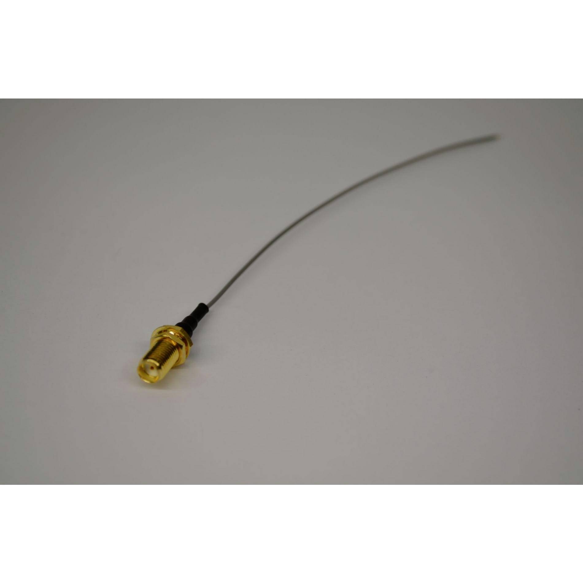 Ein dünnes, flexibles Kabel mit einem Goldstecker oder einer Goldverschraubung an einem Ende, das auf einer hellgrauen Oberfläche liegt.