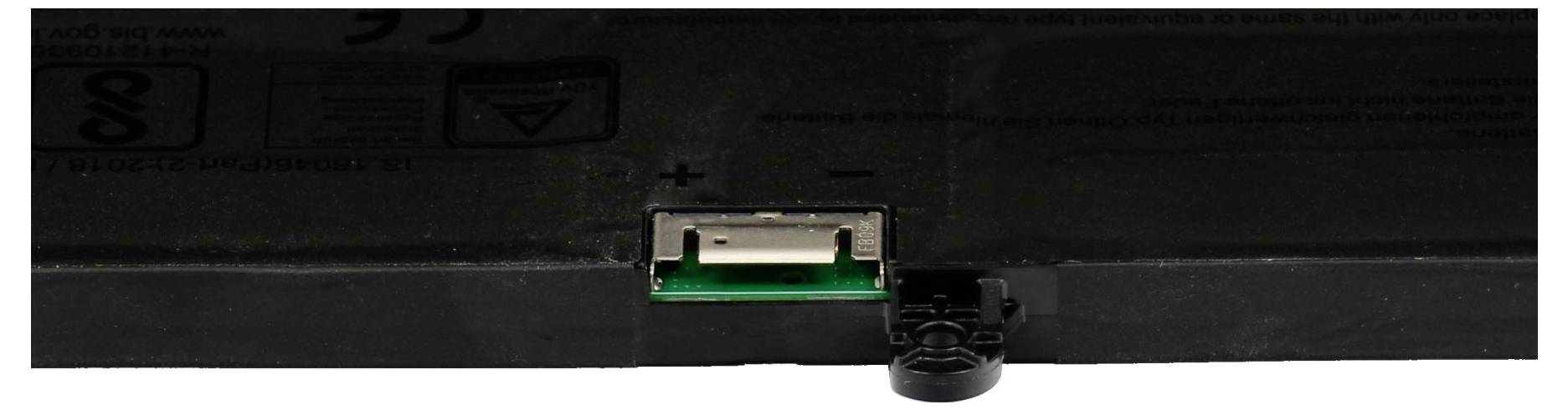 Nahaufnahme eines hinteren Anschlussbereichs eines Geräts, das einen zentralen weißen USB-Anschluss und einen nahe gelegenen schwarzen Stecker gegen ein dunkles Gehäuse zeigt.