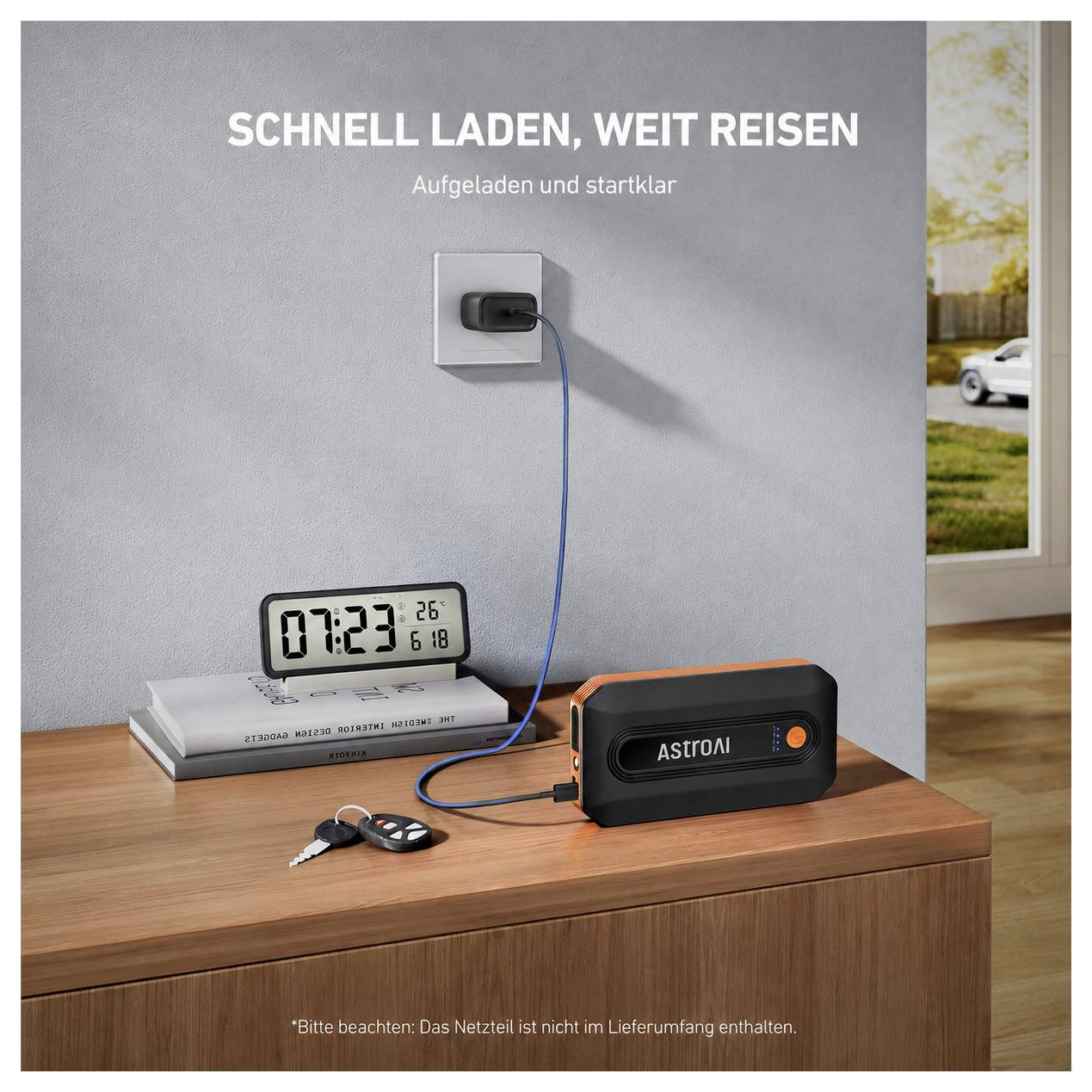 Tragbarer Astral-Starthilfegerät auf einem Holztisch, an eine Wandsteckdose angeschlossen und lädt; deutscher Text sagt „Schnell laden, weit reisen" und „Aufgeladen und startklar".