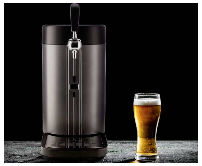 Ein Tischgetränkespender mit Zapfhahn steht neben einem gefüllten Pint-Glas mit bernsteinfarbenem Bier auf dunklem Hintergrund.