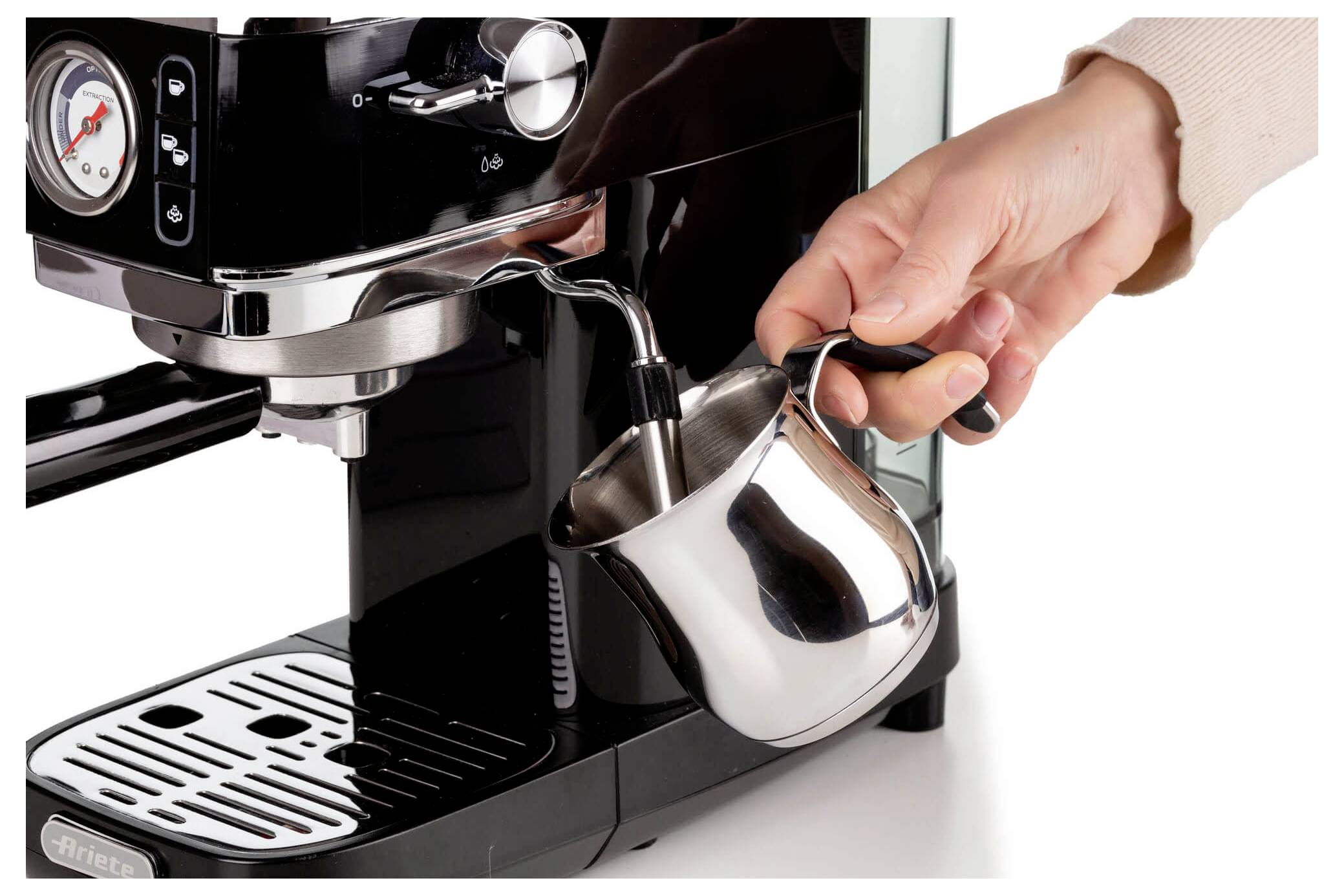 Hand, die einen Metall-Milchkrug unter die Dampflanze einer Espressomaschine hält, um Milch zu schäumen zu bereiten.