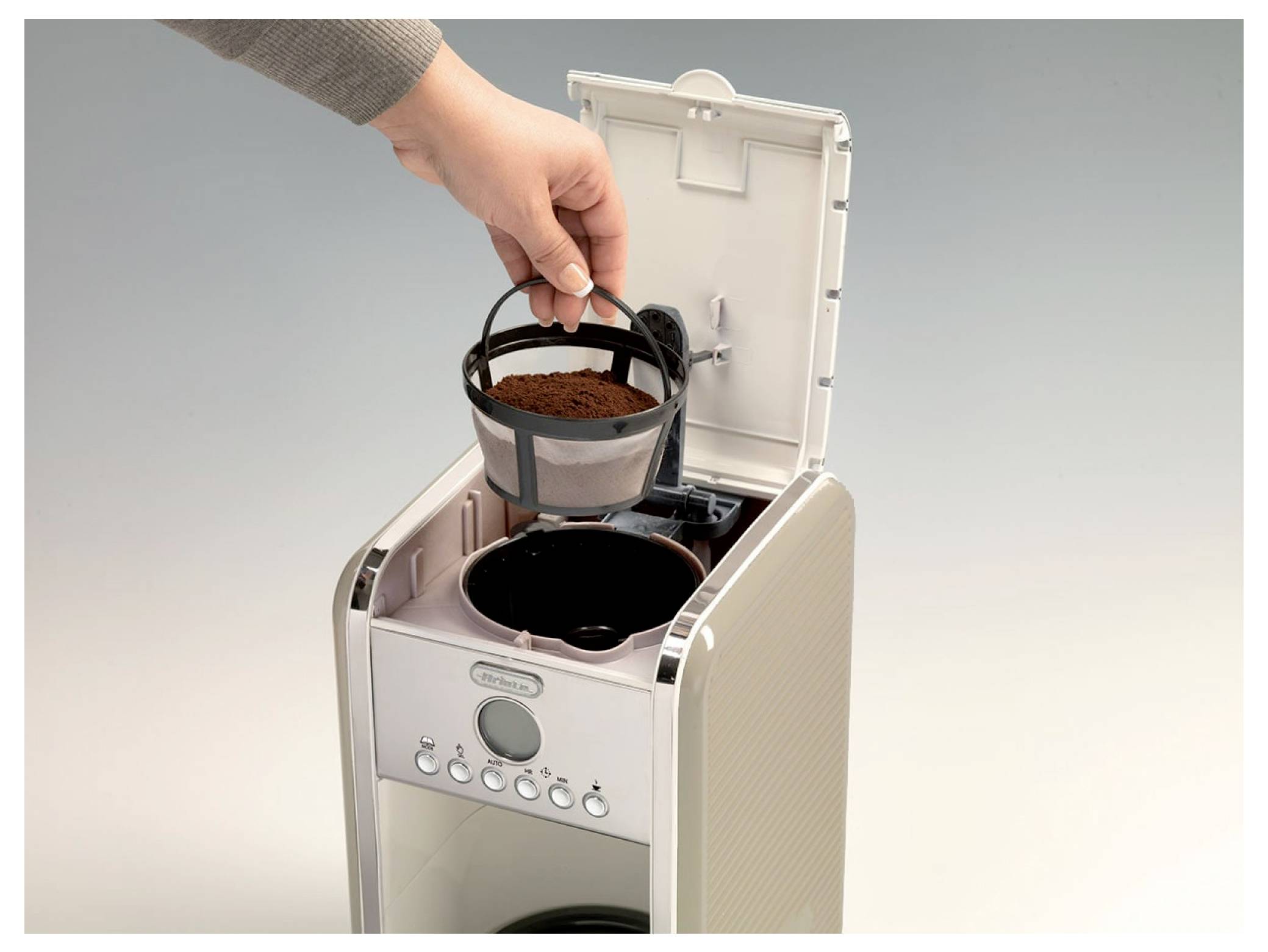 Eine Hand, die einen Kaffeefilter mit Kaffeemehl in die offene Oberseite einer Kaffeemaschine einlegt.