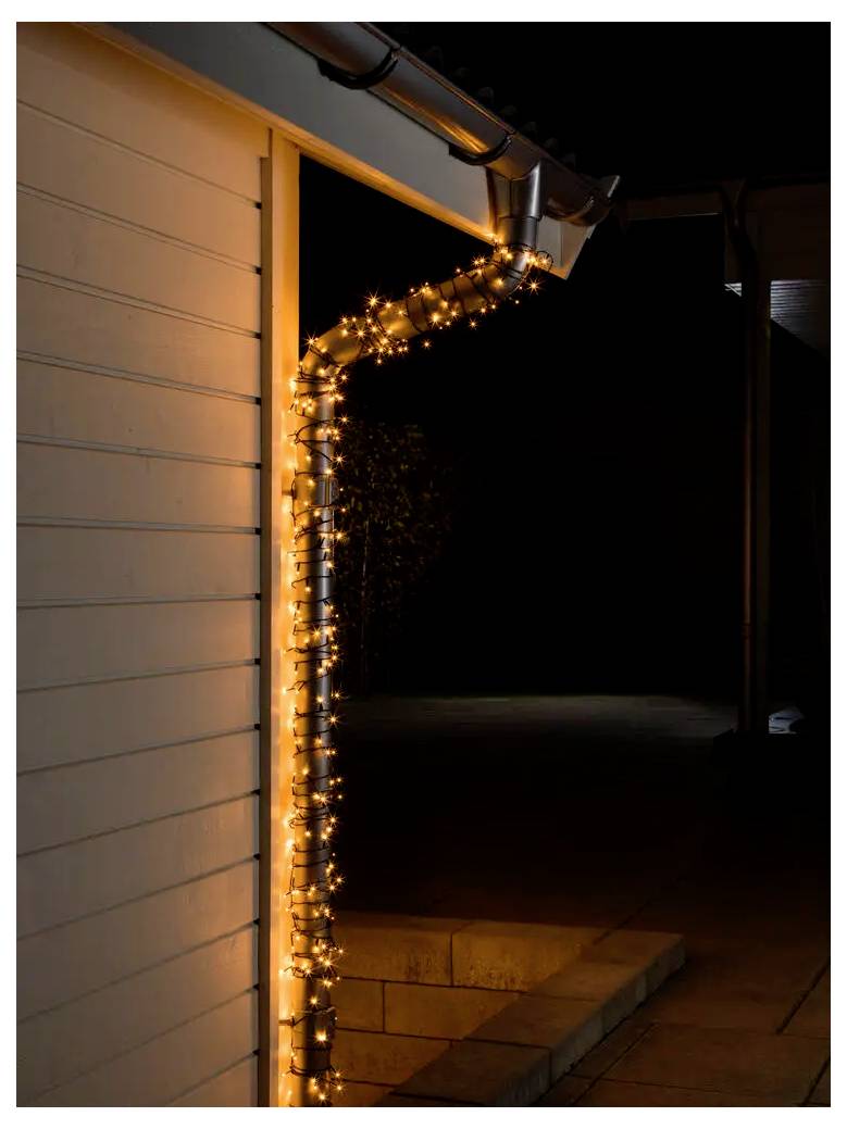 Orangefarbene Lichterketten, die um eine Hausecke und die Dachkante gewickelt sind, erleuchten einen dunklen Balkon in der Nacht.