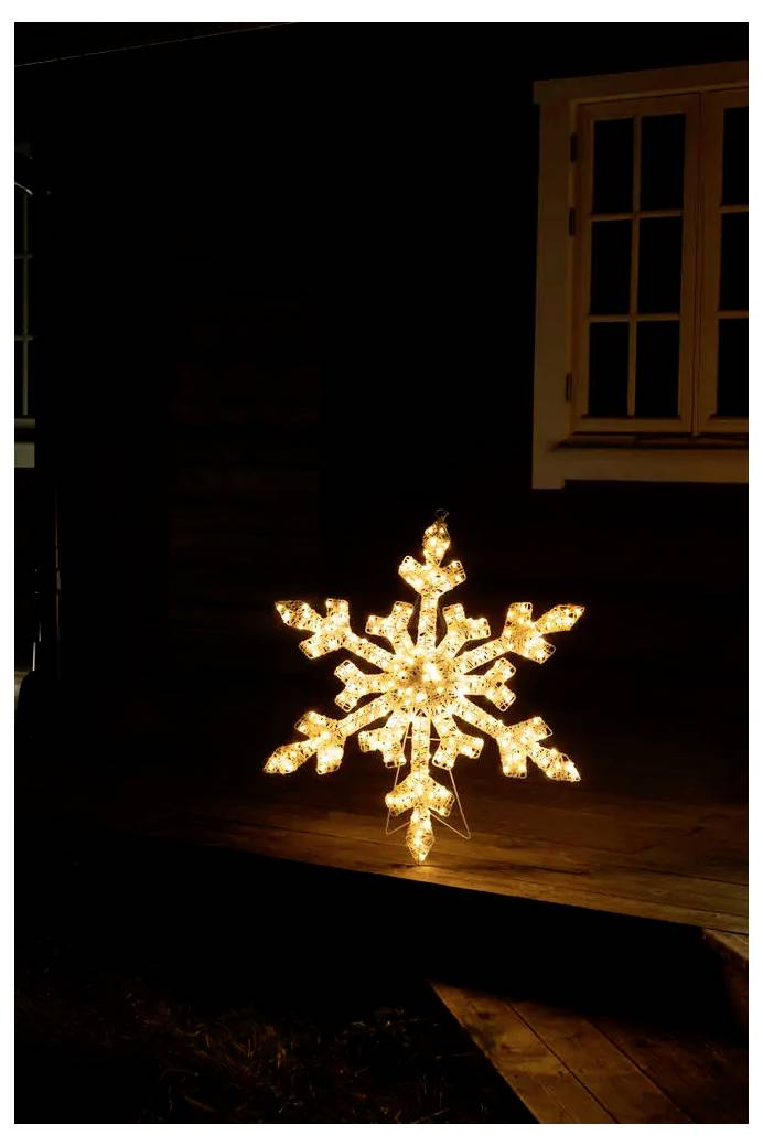 Leuchtende Schneeflocken-Dekoration, die in der Nacht auf einer hölzernen Veranda leuchtet, mit einem Fenster im dunklen Hintergrund.