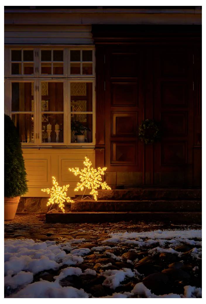 Schneebedeckter Hauseingang bei Nacht mit leuchtenden, sternenförmigen Weihnachtslichtern auf den Stufen neben einem Fenster und einer Haustür