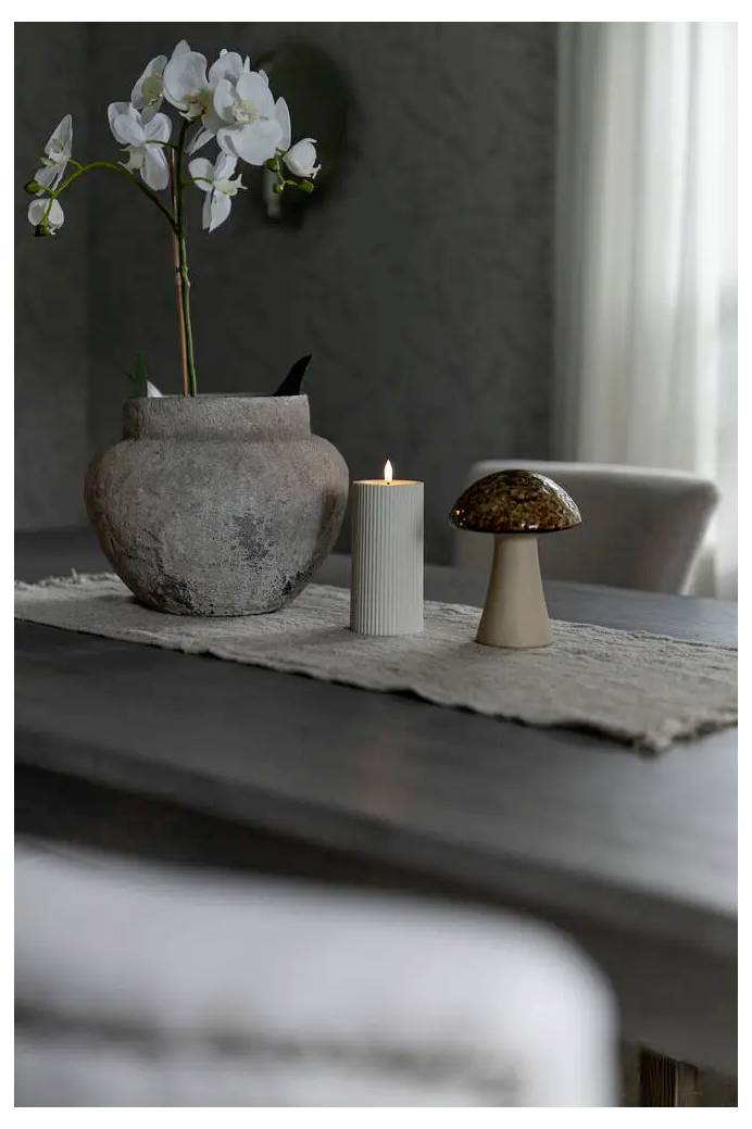 Ein grauer Tischzentnerpiece mit einer weißen Orchidee in einer Steinvase, eine brennende Kerze und ein dekoratives Pilzmodell auf einem Tischläufer in einem sanft beleuchteten Raum.