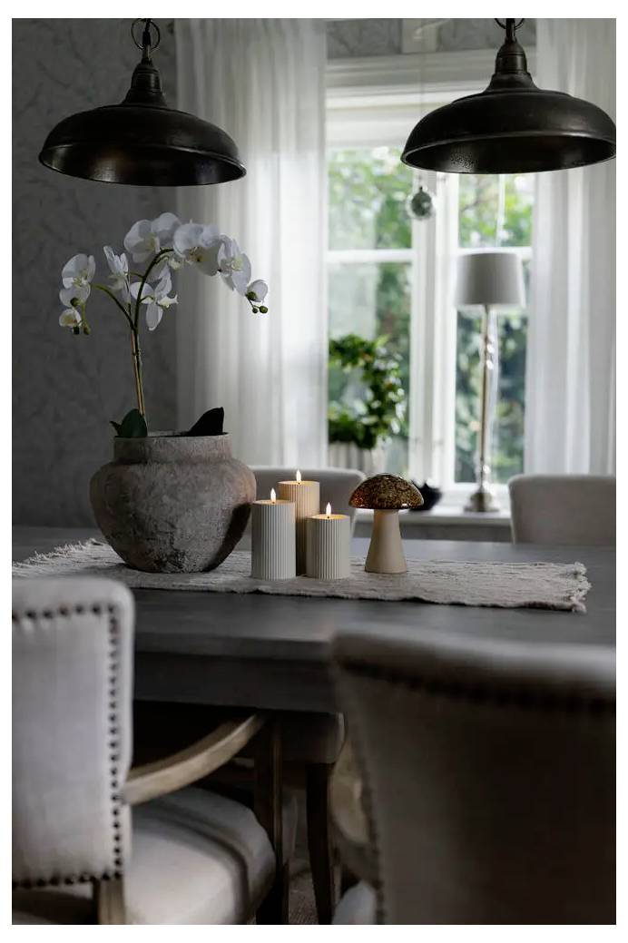 Esstisch-Mittelstück mit weißen Orchideen, Kerzen und einer pilzförmigen Lampe unter hängenden Leuchten in einem modernen Wohninterior