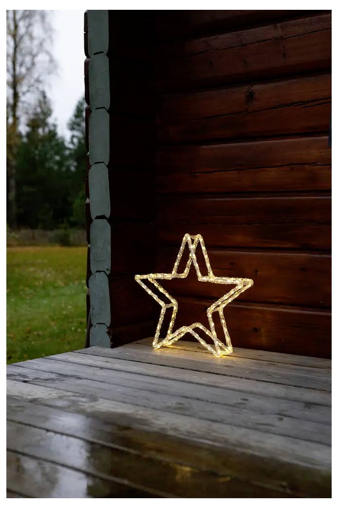 Leuchtende sternförmige Lichtdekoration auf einer Holzveranda neben einer Blockwand, mit grünem Außenbereich im Hintergrund.