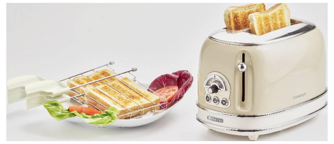 Ein Toaster mit zwei Toastscheiben springt neben einem Teller mit getostetem Brot, Salatgrün und Salamischeiben auf.